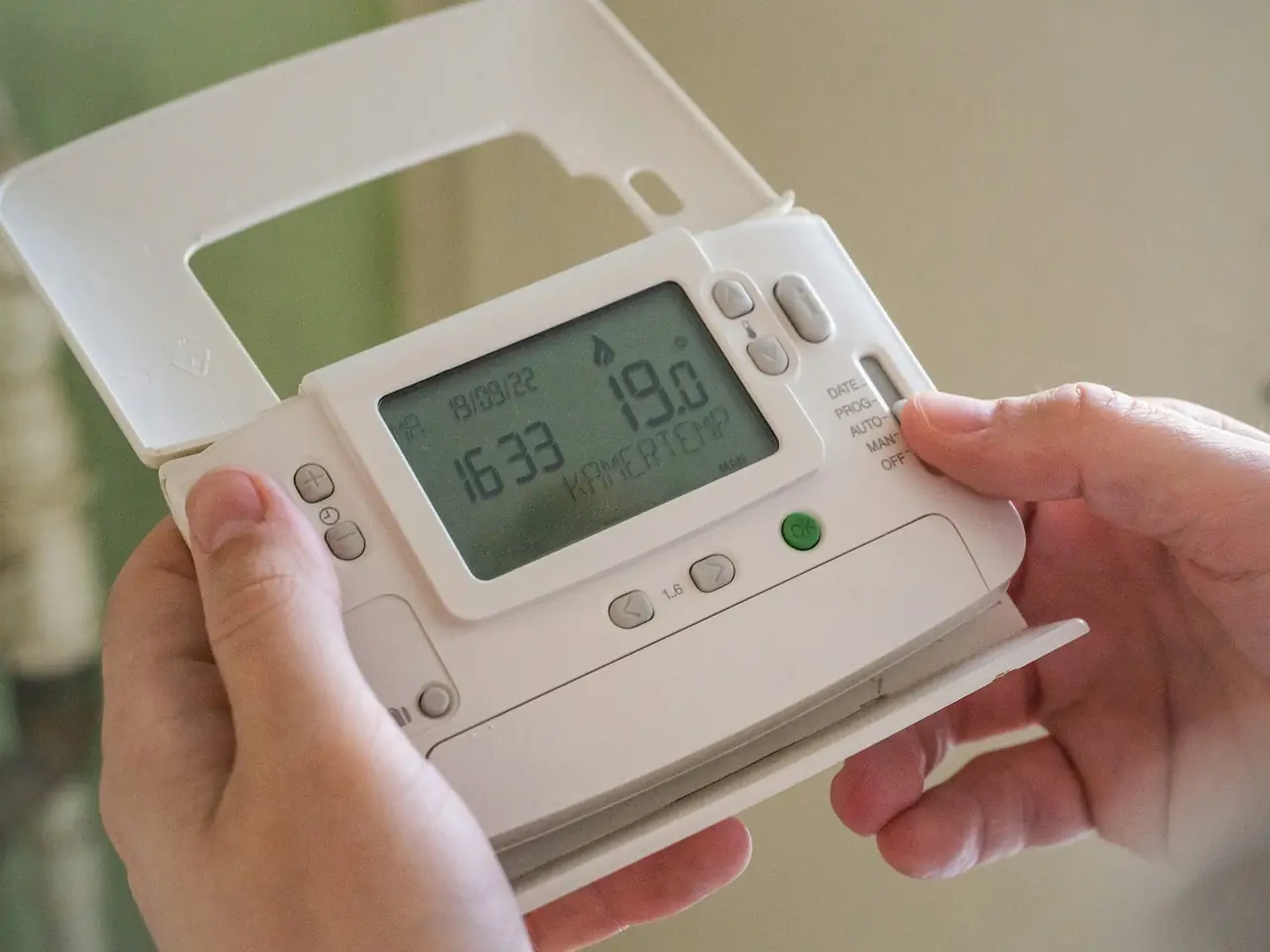 Hands holding a programmable thermostat removed from its wall plate
